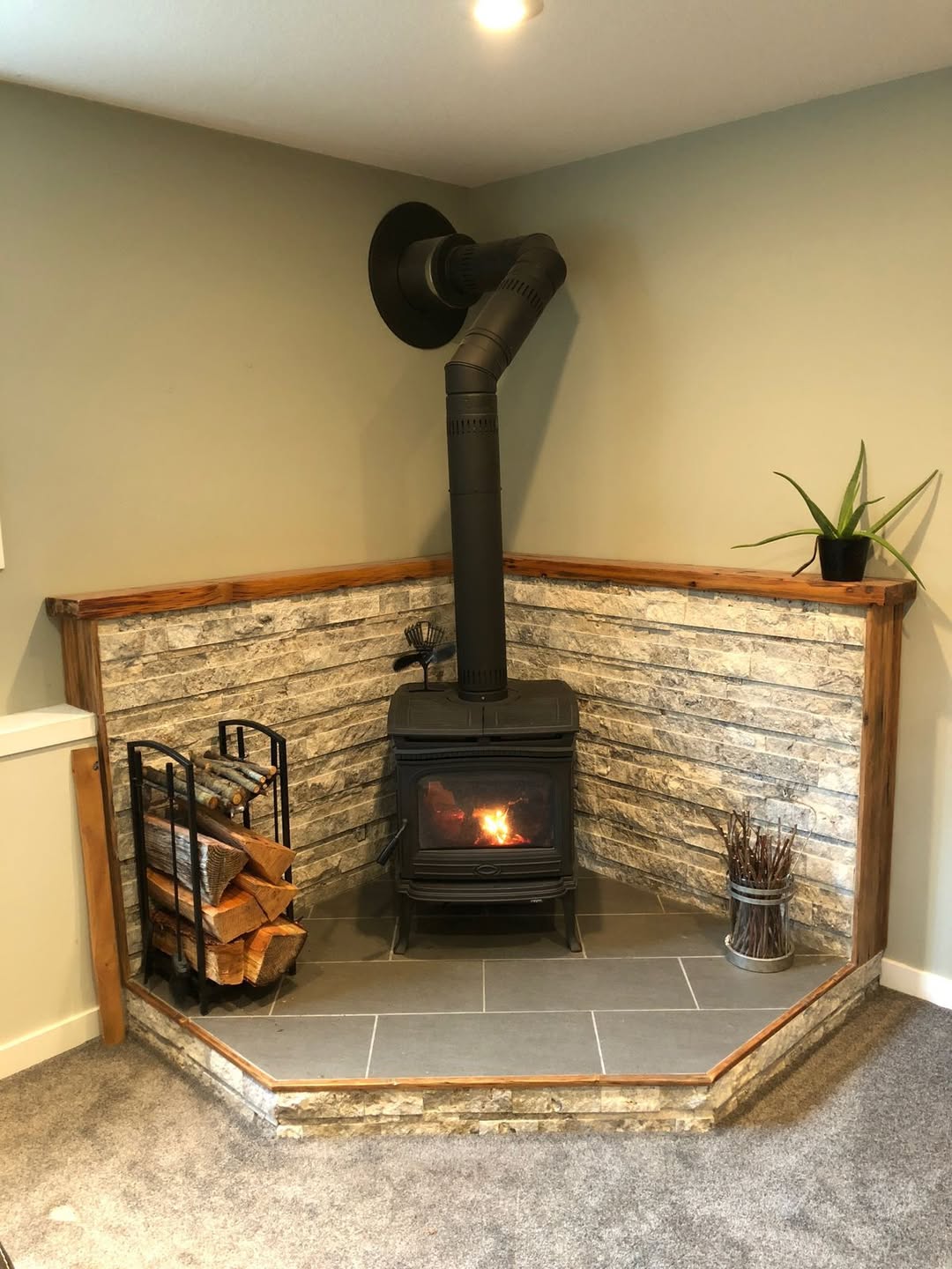 Corner wood stove with fire burning on tile hearth pad with stone surround in a Vermont home inspected by Mad River Valley Chimney Services